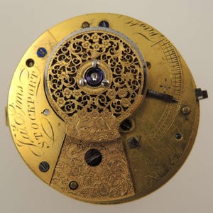 May include: Close-up of a vintage watch movement with intricate gold filigree and floral patterns. The watch mechanism features a central jewel, engraved details, and the inscription "Ja. Sims STOCKPORT".