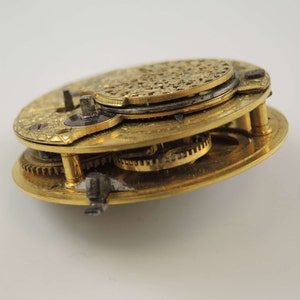 Op de afbeelding: Close-up van een goudkleurig zakhorlogemechanisme met ingewikkelde tandwielen en een decoratieve achterplaat.