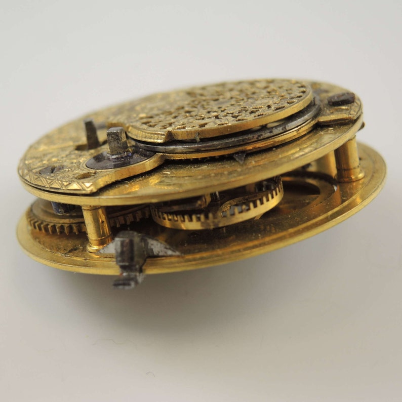 Op de afbeelding: Close-up van een goudkleurig zakhorlogemechanisme met ingewikkelde tandwielen en een decoratieve achterplaat.