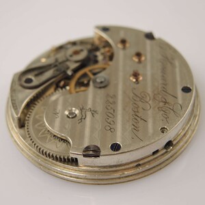 K&ouml;nnte beinhalten: Nahaufnahme der R&uuml;ckseite einer silbernen Taschenuhr mit der Inschrift "Howard & Co. Boston" und der Nummer "225098". Die Uhr hat ein sichtbares Getriebe.