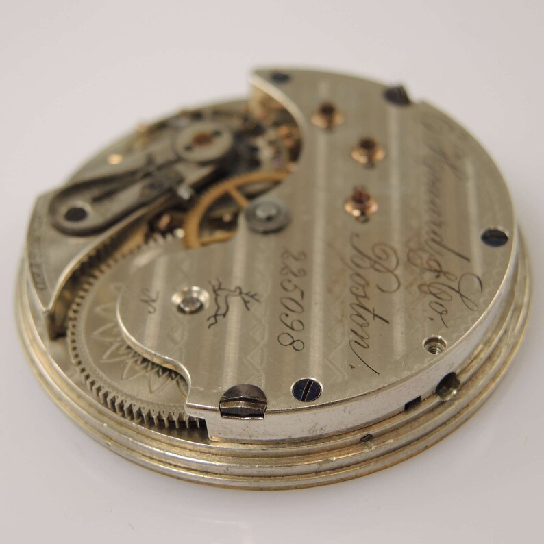 K&ouml;nnte beinhalten: Nahaufnahme der R&uuml;ckseite einer silbernen Taschenuhr mit der Inschrift "Howard & Co. Boston" und der Nummer "225098". Die Uhr hat ein sichtbares Getriebe.