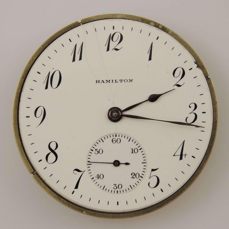 May include: A vintage Hamilton pocket watch face with a white background, black numerals, and black hands. The watch face has a subdial for seconds and the word "HAMILTON" is printed at the top.