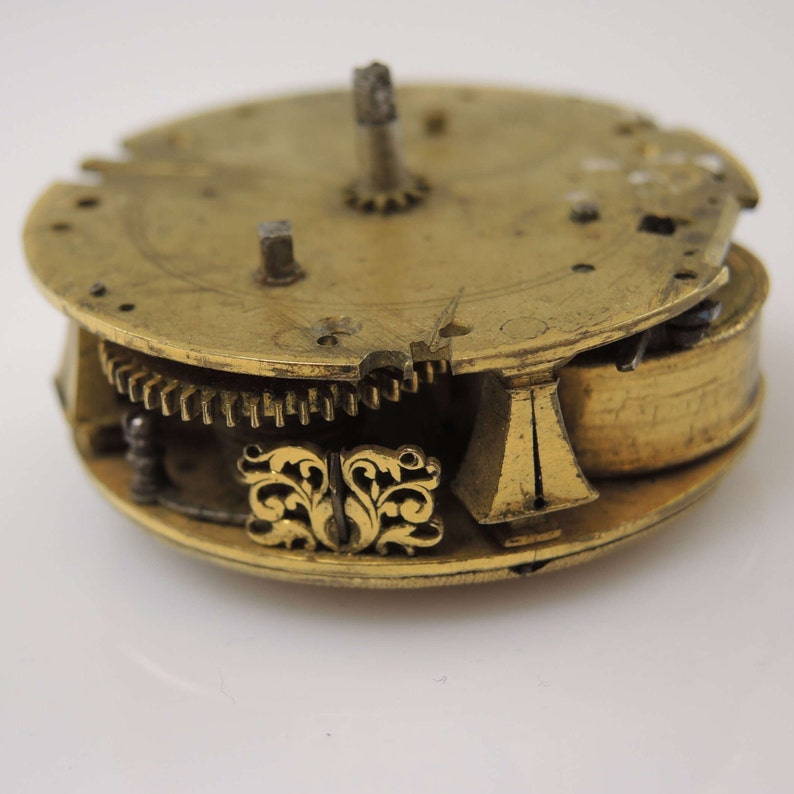 May include: Close-up of a gold-toned clock mechanism with intricate gears and a decorative floral design.