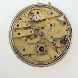 Op de afbeelding: Close-up van de ingewikkelde binnenkant van een gouden zakhorloge. Het uurwerk is zichtbaar en toont een complexe opstelling van tandwielen en veren.