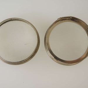 Puede incluir: Dos anillos de metal plateado, uno abierto y otro cerrado, con una superficie lisa y brillante.