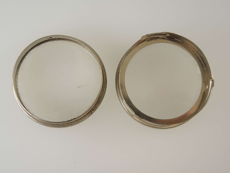 Puede incluir: Dos anillos de metal plateado, uno abierto y otro cerrado, con una superficie lisa y brillante.