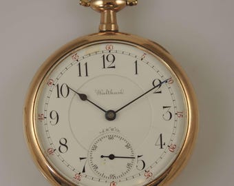 Puede incluir: Un reloj de bolsillo de oro con una esfera blanca y agujas negras. El reloj tiene marcadores de hora en números romanos y marcadores de minutos en números arábigos. La esfera del reloj también tiene la palabra "Waltham" impresa en ella.