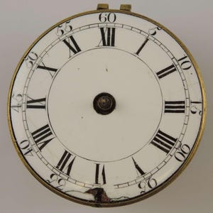 May include: A white clock face with black Roman numeral hour markers and black minute markers. The clock face is surrounded by a brass bezel with numbers 5, 10, 15, 20, 25, 30, 35, 40, 45, 50, 55, and 60.