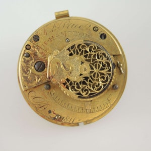 K&ouml;nnte beinhalten: Nahaufnahme eines Vintage-Taschenuhrwerks. Der goldfarbene Mechanismus weist komplizierte Details auf, darunter Zahnr&auml;der, Schrauben und eine dekorative Filigranarbeit. Die Uhr ist mit Text und dem Jahr 1811 beschriftet.