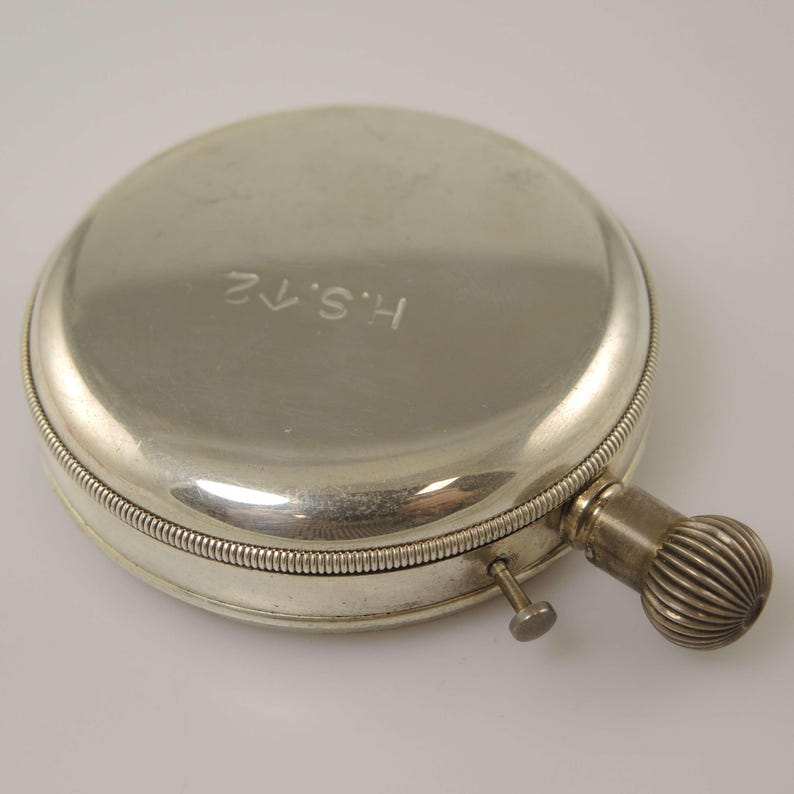 K&ouml;nnte beinhalten: Eine silberfarbene, runde Taschenuhr mit strukturiertem Aufzugsknopf und kleinem Knopf. Die Uhr hat die eingravierten Initialen "H.S.12" auf dem Deckel. Die Uhr ist ein Vintage-Artikel.