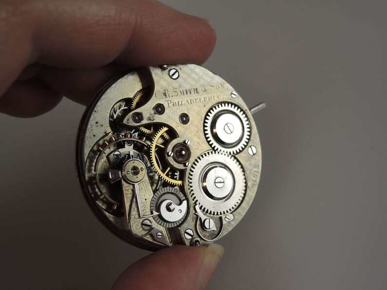 May include: Close-up of a silver pocket watch movement with intricate gears and the inscription "C.F. Smith & Son, Philadelphia".