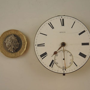May include: A white pocket watch face with black Roman numeral hour markers and black minute markers. The watch face has a small seconds dial at the 6 o'clock position. The watch face has the number 45779 printed on it.