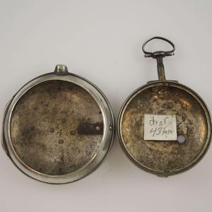 Könnte beinhalten: Die Rückseite einer silbernen Taschenuhr mit einem 43 mm Zifferblatt. Die Uhr ist geöffnet und das Innere des Gehäuses ist sichtbar. Die Uhr hat einen Schlüsselzug.