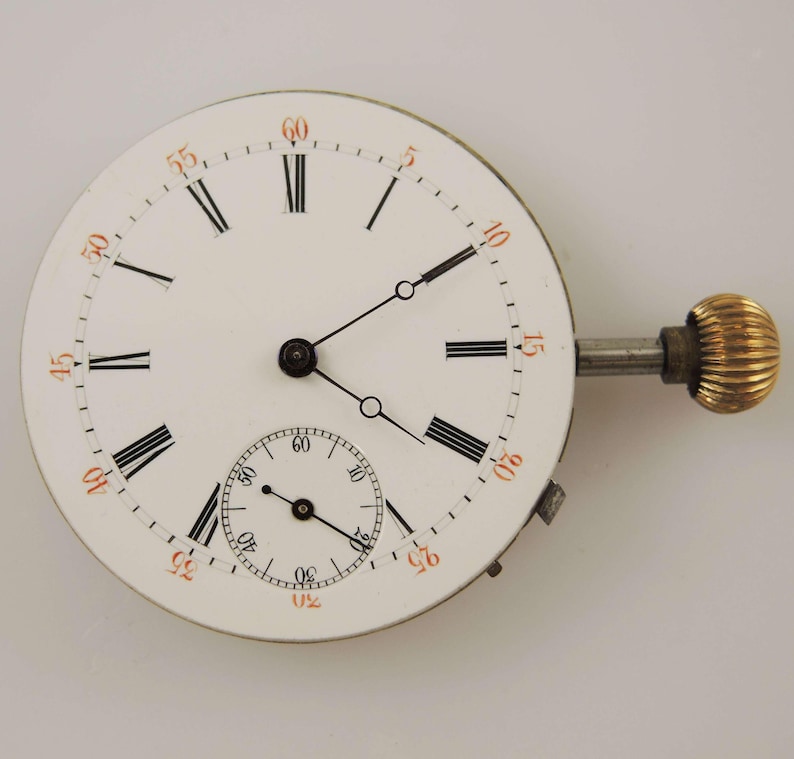 May include: A vintage watch face with a white background, black Roman numerals, and a smaller seconds dial. The minute markers are in orange. The watch has a silver stem and a gold-colored crown.