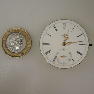 May include: A white pocket watch with Roman numeral hour markers and black hands. The watch has a smaller, circular subdial with black markings.