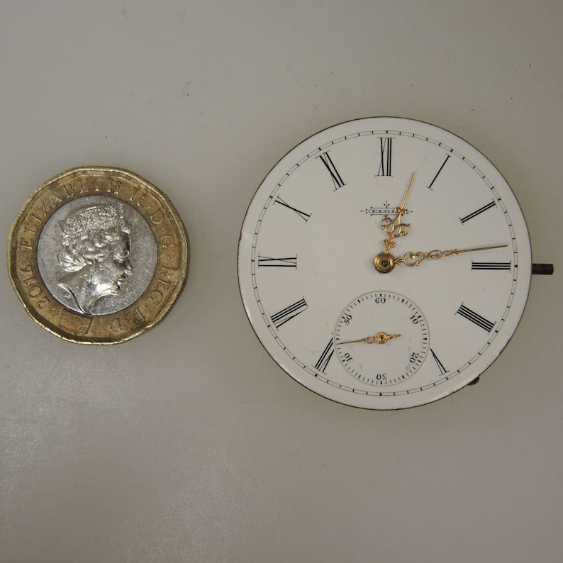 May include: A white pocket watch with Roman numeral hour markers and black hands. The watch has a smaller, circular subdial with black markings.