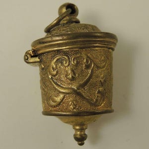 May include: A gold-toned metal thimble with an ornate design and a hinged lid. The thimble has a loop at the top for hanging.