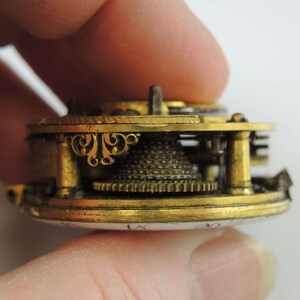 May include: Close-up of a gold-toned pocket watch mechanism with intricate details. The watch face is visible with the numbers 15 and 20.