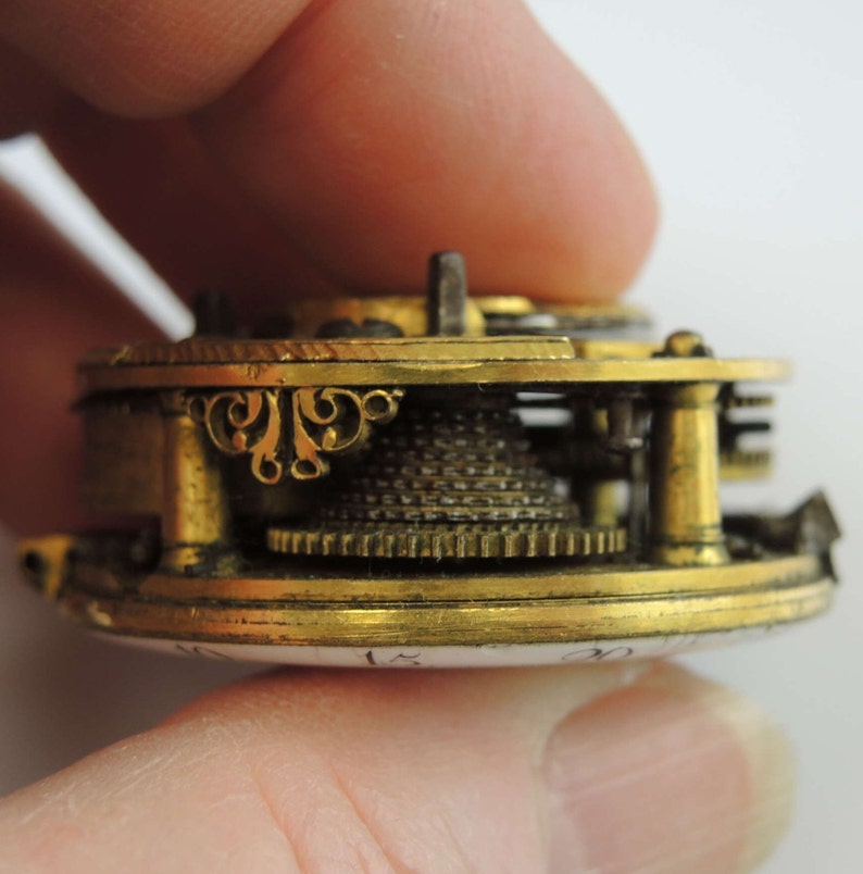 May include: Close-up of a gold-toned pocket watch mechanism with intricate details. The watch face is visible with the numbers 15 and 20.