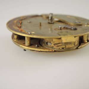 K&ouml;nnte beinhalten: Nahaufnahme eines Vintage-Uhrwerks, das seine inneren Mechanismen zeigt. Die Messingkomponenten weisen Alterserscheinungen und Rost auf, was die Geschichte der Uhr unterstreicht. Das Design umfasst Zahnr&auml;der, Hebel und andere kleine Teile.