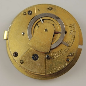 May include: A gold-colored pocket watch movement with a silver-colored adjustment ring and a slow adjustment scale. The movement has a number "6320" engraved on the bottom.
