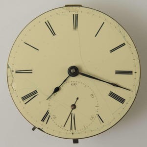 May include: Antique pocket watch face with a cream-colored dial and black Roman numerals. The watch face has two smaller dials and black hands. The face is cracked, showing its age. The watch face is a vintage item.