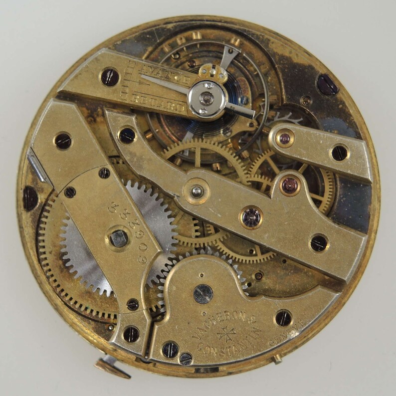 May include: Close-up of a gold-toned pocket watch movement with intricate gears and a lever. The watch is labelled "Van Berlo & Co.  Constantin" and "Swiss Made".