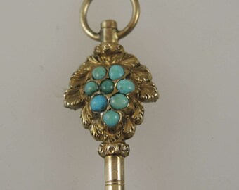 May include: Gold watch key with a cluster of turquoise stones set in a leaf design.