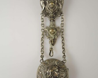 May include: An antique silver pocket watch with an ornate design. The watch features a detailed relief of a woman's profile, surrounded by floral and scrollwork. It hangs from a decorative chain and clasp, with an elaborate top piece.