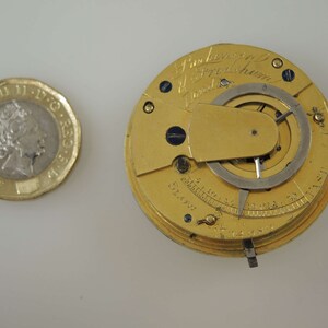 May include: A gold pocket watch with a silver dial and a lever on the side. The watch is engraved with the text "J. Parkinson & Fredshum London".
