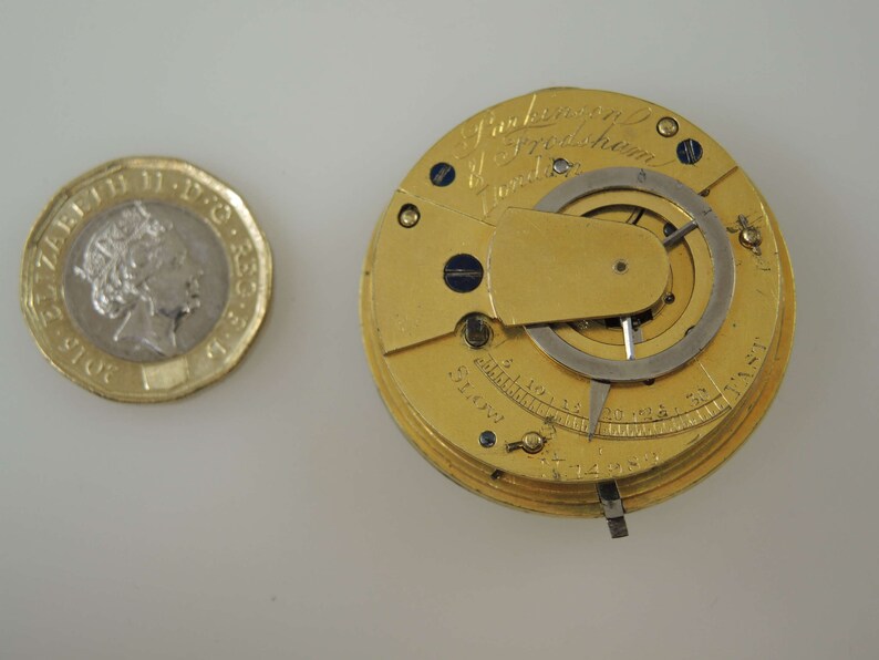 May include: A gold pocket watch with a silver dial and a lever on the side. The watch is engraved with the text "J. Parkinson & Fredshum London".