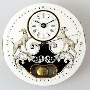 May include: A round white clock face featuring a smaller upper dial with black Roman numerals and thin hands. Two grey dog illustrations flank a central black scrollwork design. A brass-colored circular component sits at the bottom center.