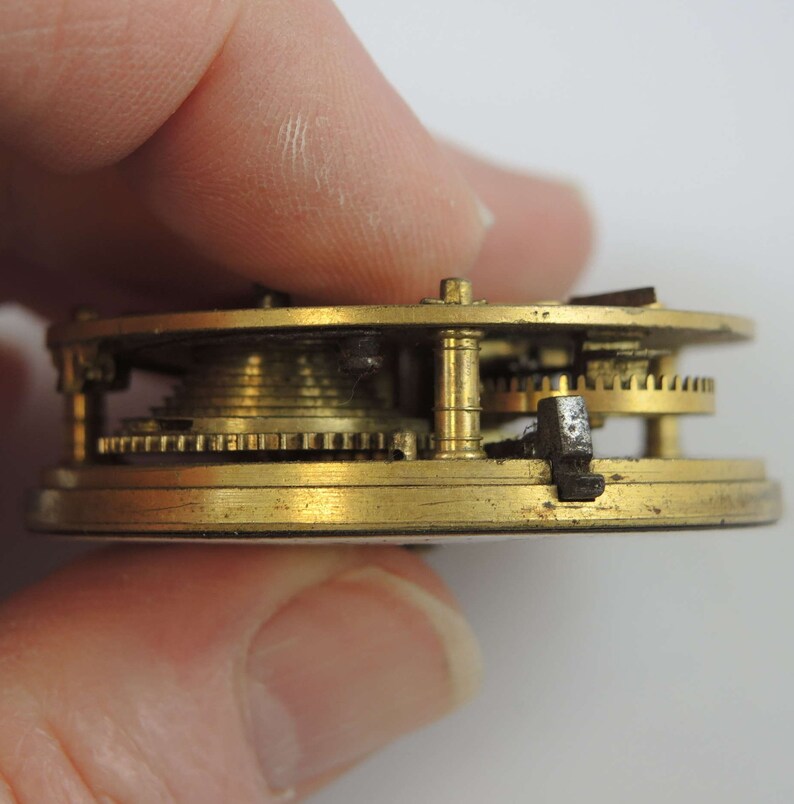 May include: Close-up side view of a brass pocket watch mechanism with intricate gears and a black metal lever.