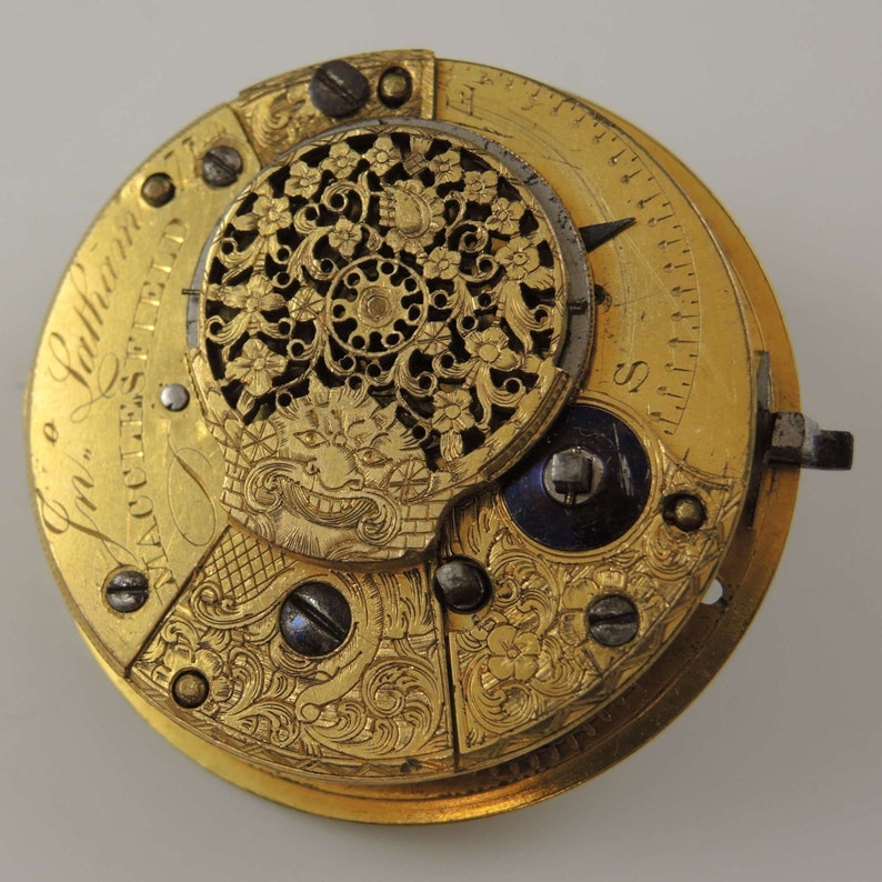 Op de afbeelding: Een gouden zakhorloge met ingewikkelde gravures en een gedetailleerd bloemmotief. Het horloge gezicht is zichtbaar met Romeinse cijfers en een kleine hand. Het horloge is in een perfecte staat.