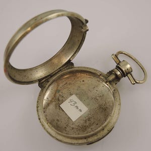 Könnte beinhalten: Silberne Taschenuhr mit einem aufklappbaren Deckel, der das Innere des Uhrengehäuses freilegt. Die Uhr hat einen Durchmesser von 43 mm.