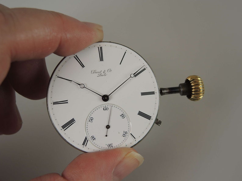 May include: A white pocket watch face with black Roman numeral hour markers and black hands. The watch face has the text "Dent & Co. London" printed on it. The watch has a gold winding stem.