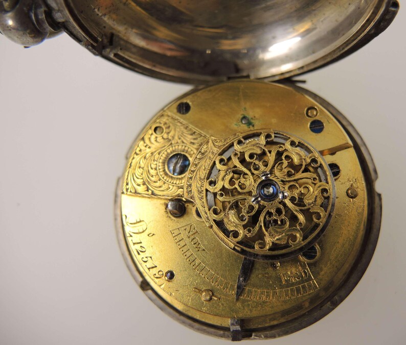 May include: Open pocket watch with a silver case and a gold-toned movement. The movement features intricate filigree and engraved details, including the number "12519". The watch is partially open, revealing the internal mechanisms.