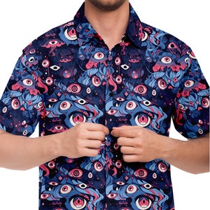 May include: A blue and pink short-sleeved button-up shirt with a repeating pattern of eyes. The shirt has a dark blue background with pink and blue eyes, and a white collar.