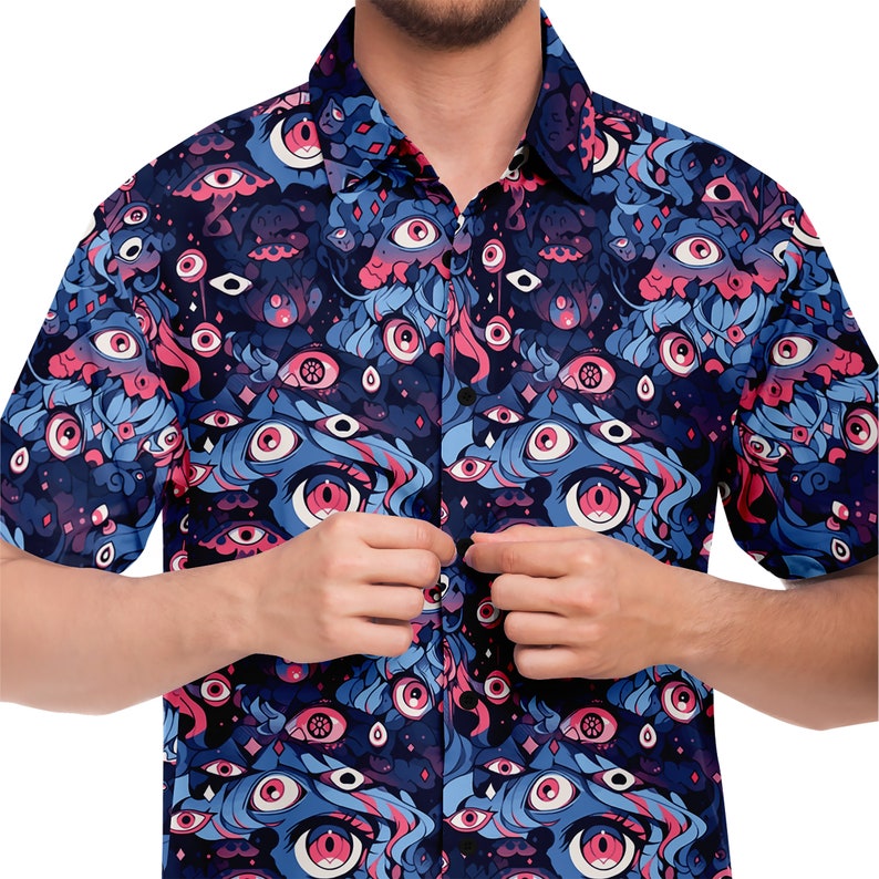 May include: A blue and pink short-sleeved button-up shirt with a repeating pattern of eyes. The shirt has a dark blue background with pink and blue eyes, and a white collar.