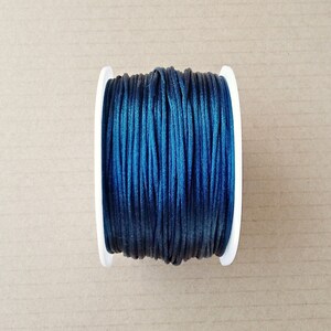 Può includere: Un rocchetto di cordoncino cerato blu scuro, avvolto su un'bobina di plastica bianca.