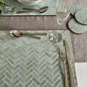 May include: Green and white patterned placemat with a silver fork and knife, and a silver spoon. The placemat is made of a woven material and has a herringbone pattern.