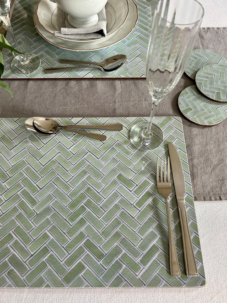 May include: Green and white patterned placemat with a silver fork and knife, and a silver spoon. The placemat is made of a woven material and has a herringbone pattern.