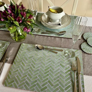 May include: A green and white patterned placemat with a herringbone design. The placemat is set with a fork, knife, spoon, and a glass of water.