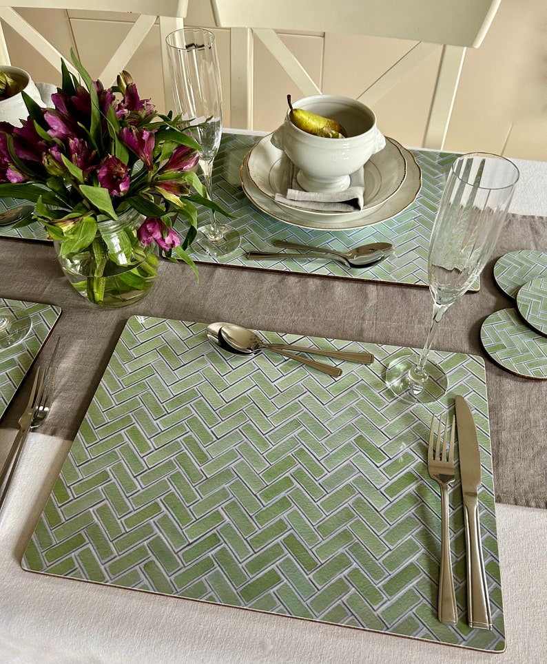 May include: A green and white patterned placemat with a herringbone design. The placemat is set with a fork, knife, spoon, and a glass of water.