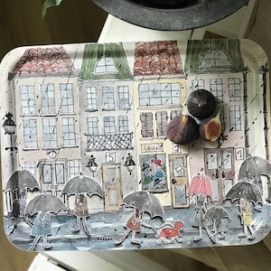 Pode incluir: Uma bandeja branca com uma ilustração colorida de uma cena de rua com edifícios, guarda-chuvas e pessoas. A bandeja tem um design caprichoso e é perfeita para servir lanches ou bebidas.