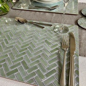 May include: A green and white patterned placemat with a herringbone design. A fork, knife, and spoon are placed on the placemat.