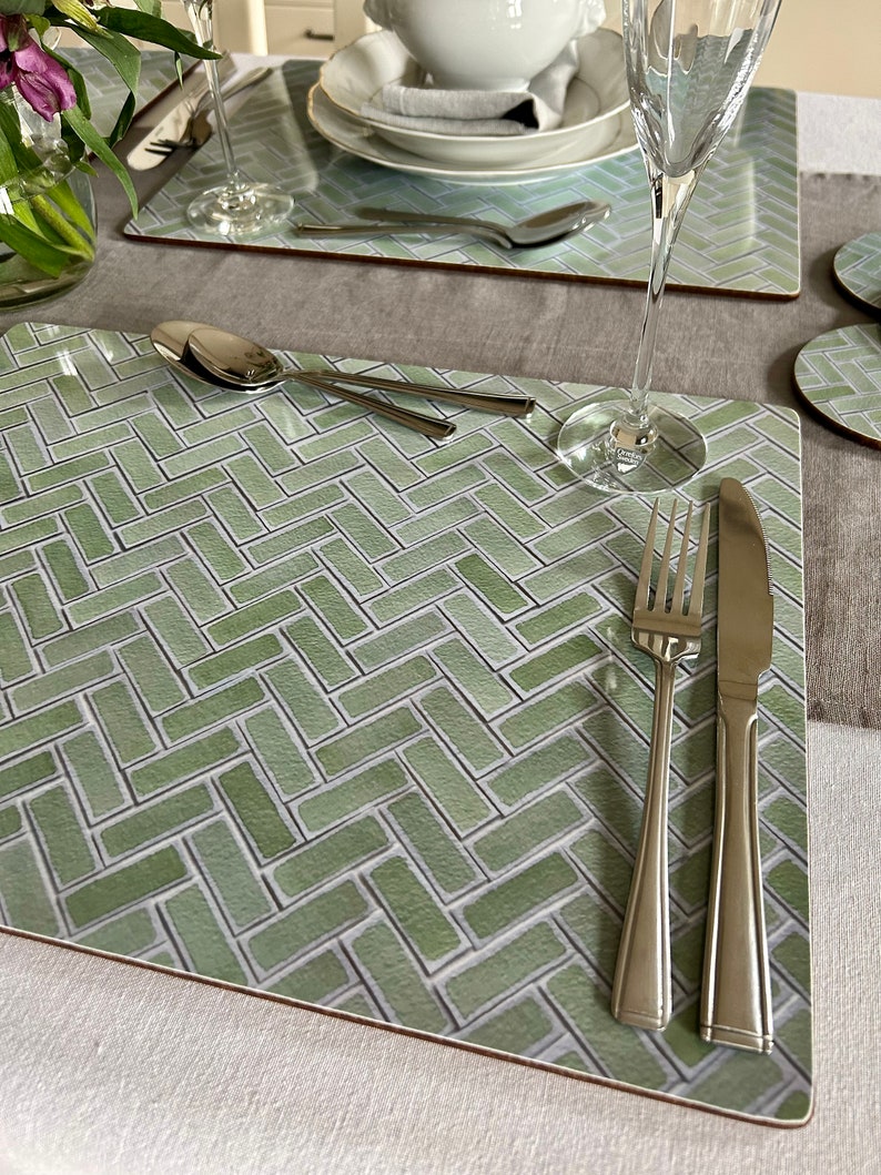 May include: A green and white patterned placemat with a herringbone design. A fork, knife, and spoon are placed on the placemat.