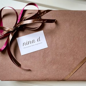 May include: A brown paper package tied with a burgundy and brown ribbon. The package is labeled with a white card that reads "nina d illustration + home inspiration".