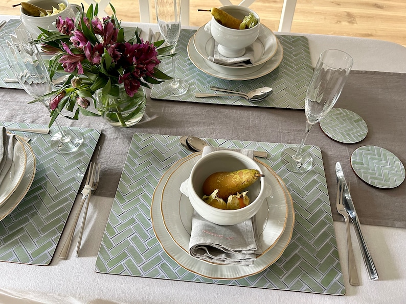May include: A table setting with two place settings featuring white bowls with pears and a green and white patterned placemat. The placemats have a herringbone pattern.