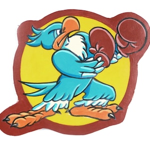 Op de afbeelding: Een cartoon illustratie van een blauwe vogel met bokshandschoenen, tegen een gele cirkel en een rode rand. De vogel staat in een boksstand, met zijn vleugels en voeten in beweging. De vogel heeft een oranje snavel en voeten.